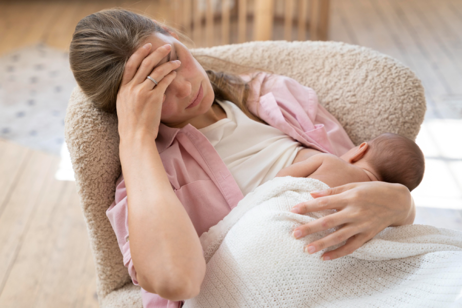 Image of a mother breastfeeding with a somber expression, depicting postpartum depression symptoms.